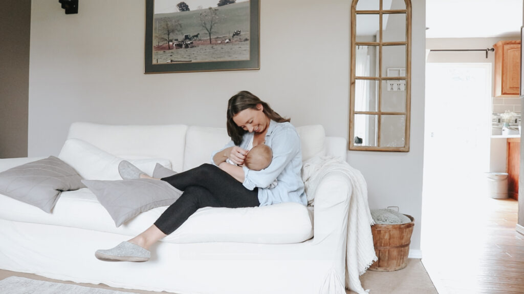 Christian homemaker plays with her baby on the couch in the living room. The couch is white.